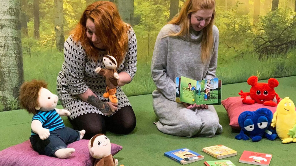 Bibliotekspersonal läser högt för mjukdjur som sitter i ring.