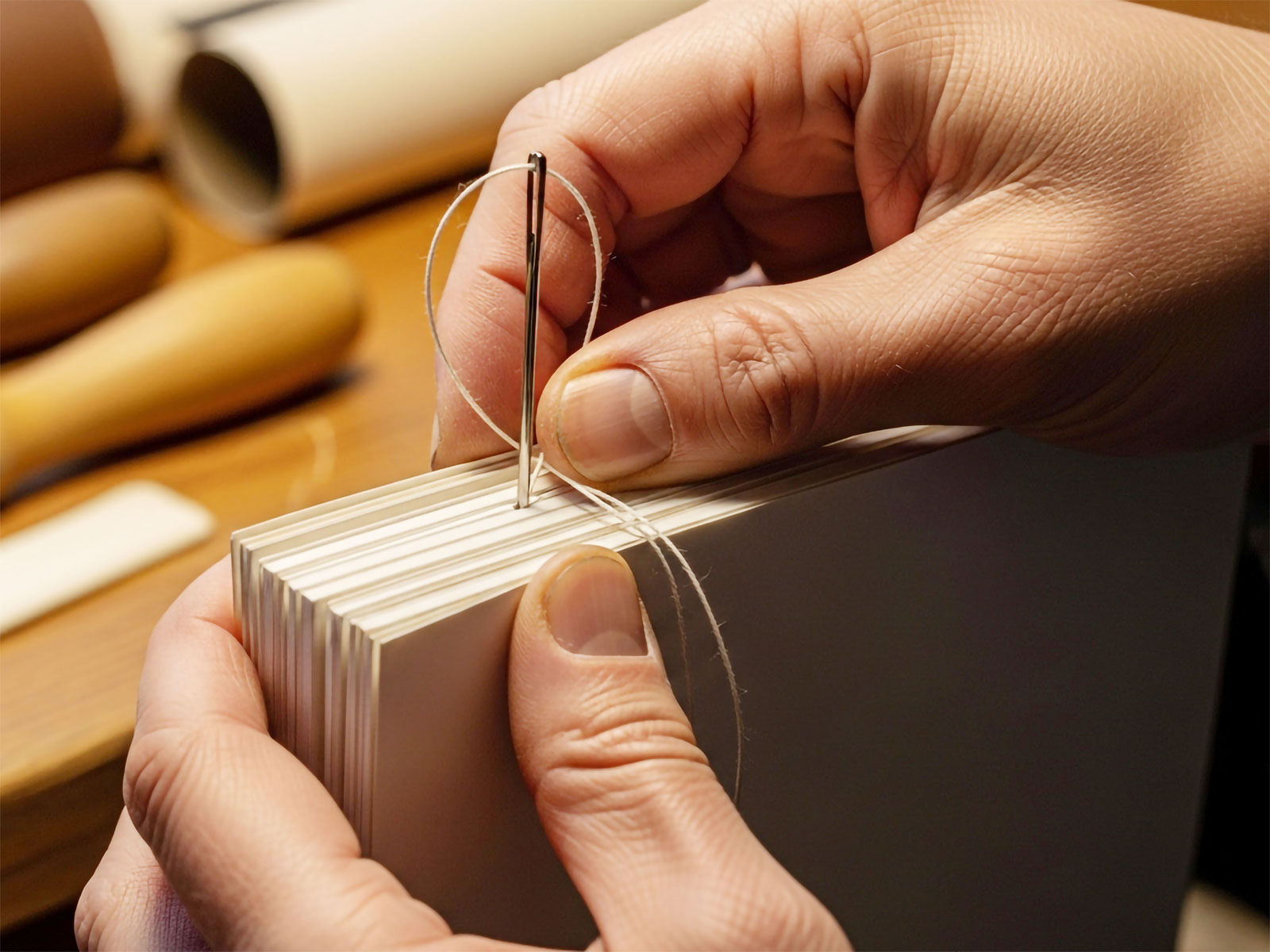 Bokbindare syr i ryggen på en bok.