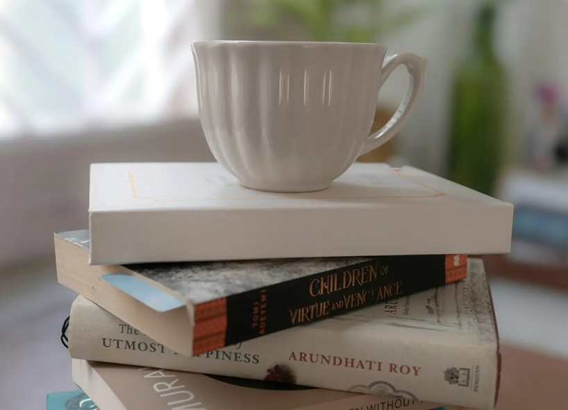 En vit kopp som balanserar på en hög med böcker.