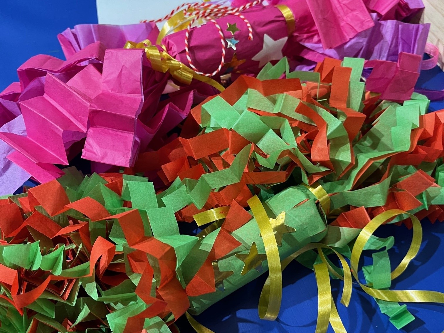 Två smällkarameller med krusade fransar i grönt, rött, rosa och lila.