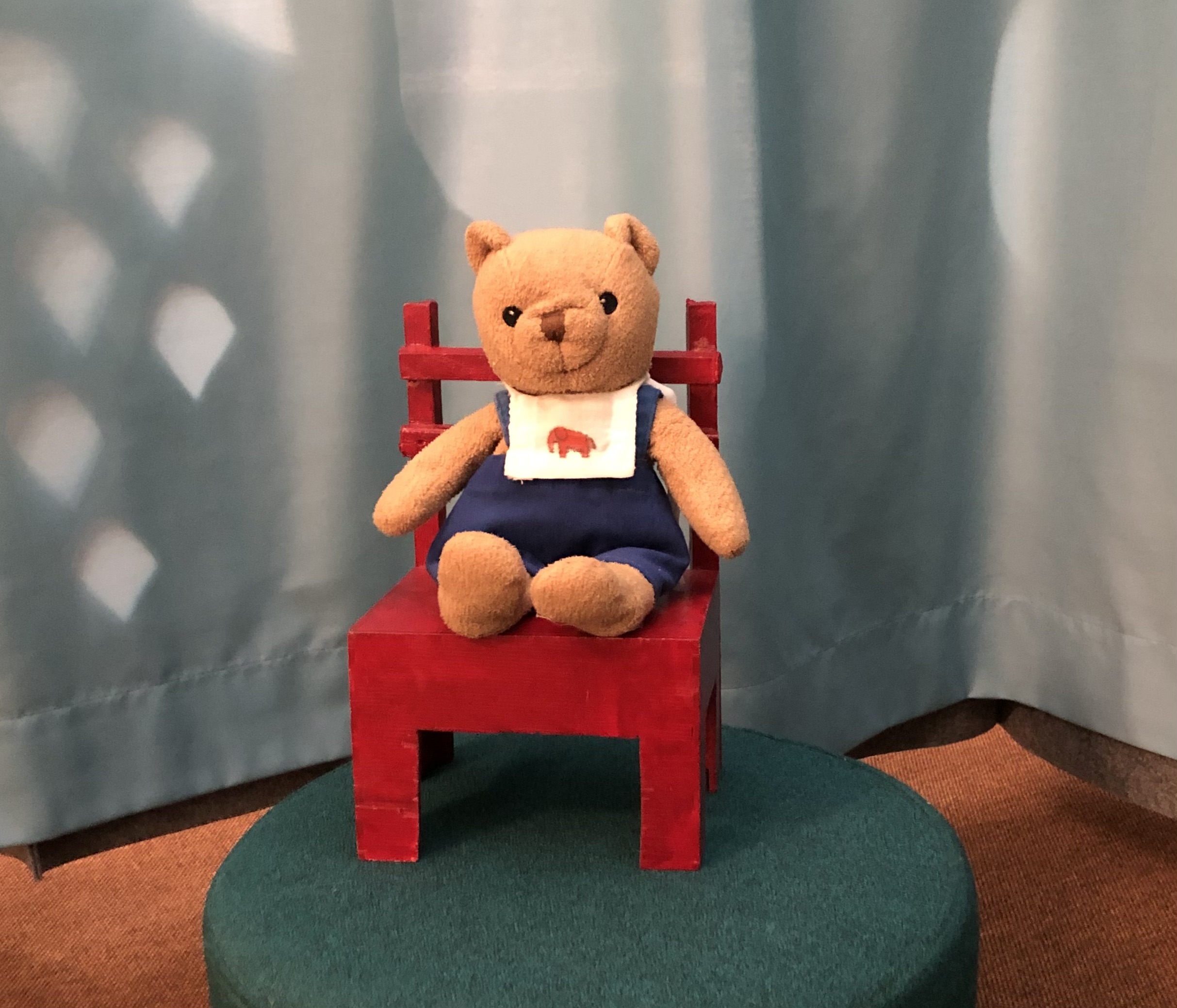 Nallebjörn med hängslen sitter på en röd stol.