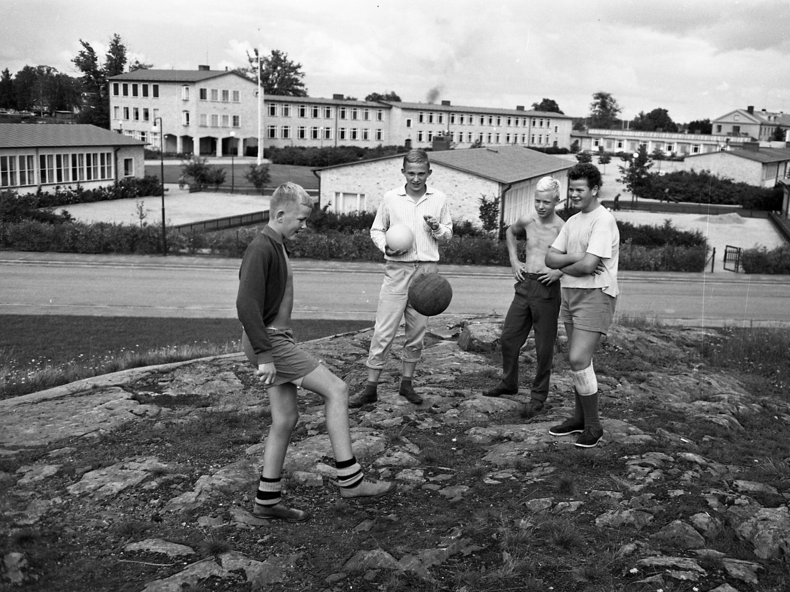Fyra pojkar står med en boll på en bergsknalle framför Gäddgårdsskolan på 1960-talet.