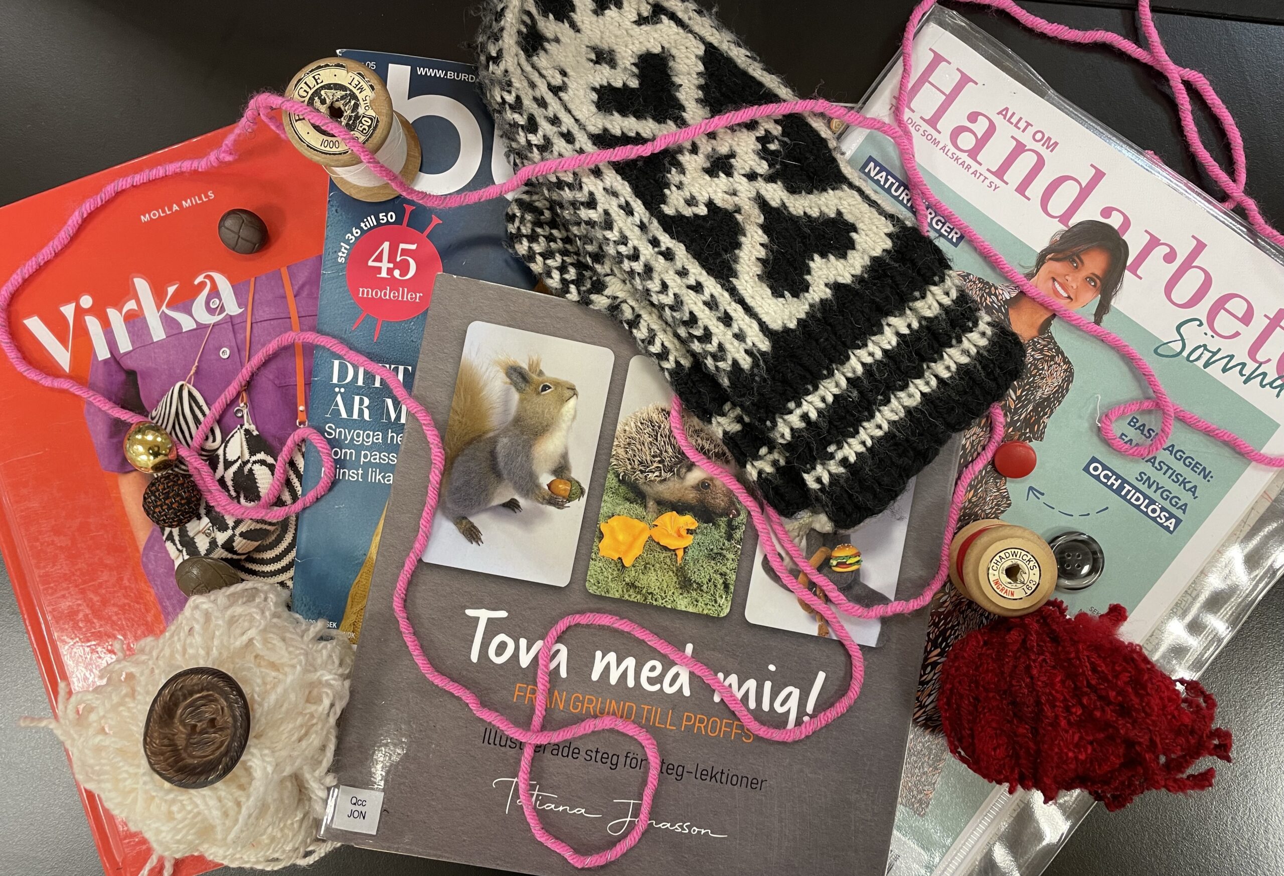 Handarbetsmaterial med garn, stickad mössa, knappar och handarbetstidningar.