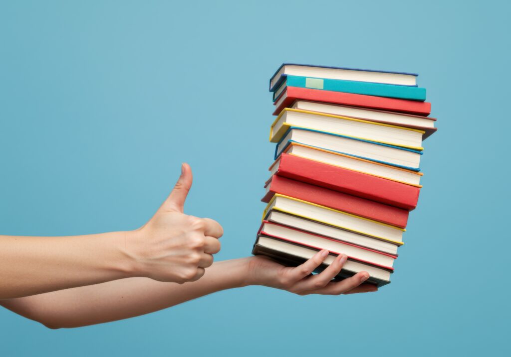 Hand holding a stack of books and giving thumbs up