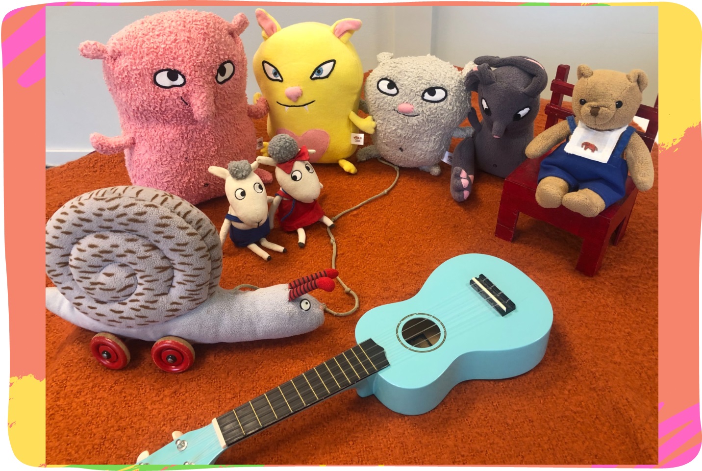 Bild på samling av flera gosedjur - en snigel, en nalle, två får och flera fantasidjur - och en ukulele