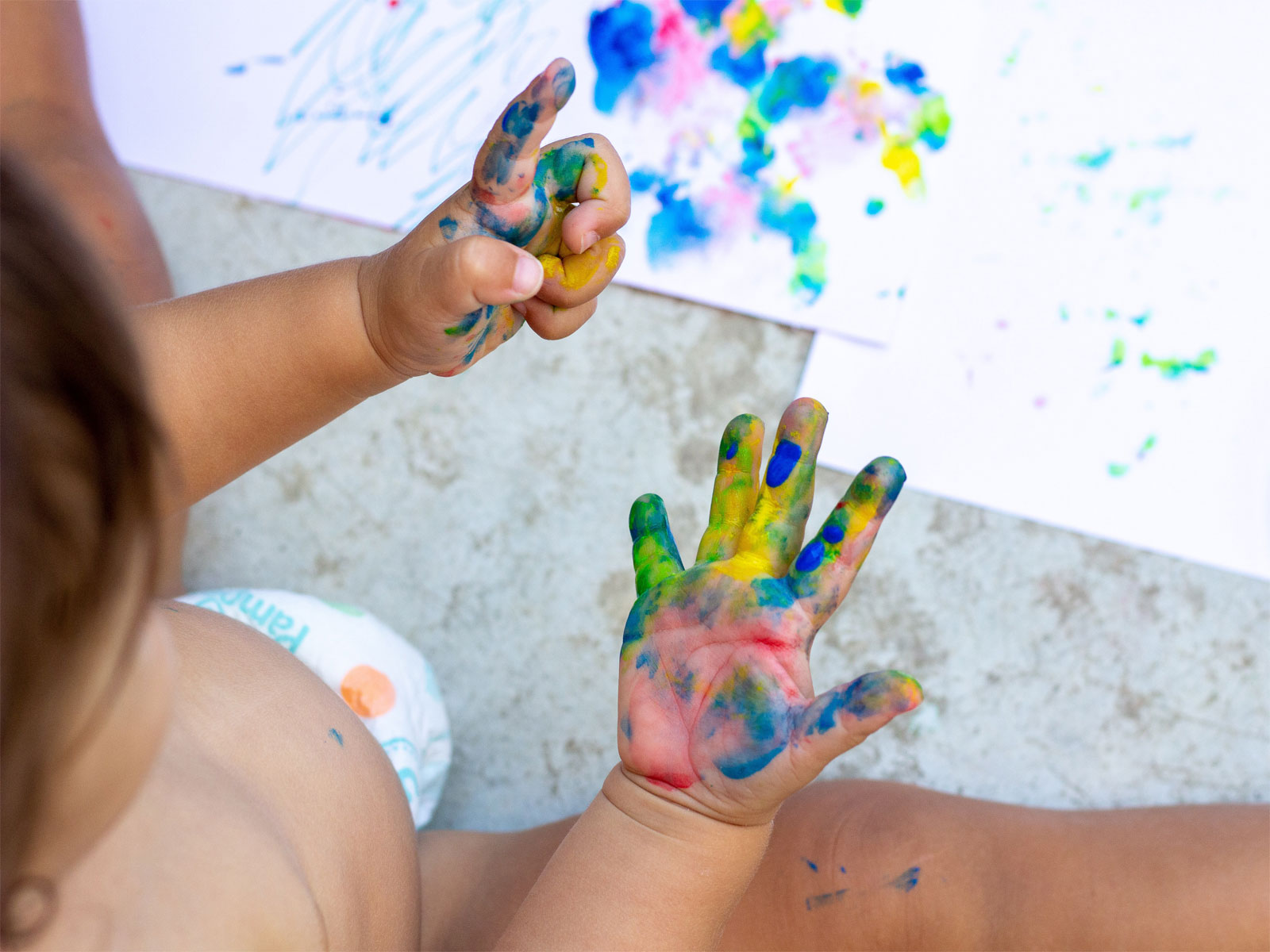 Barn i blöja som kladdar med färger.