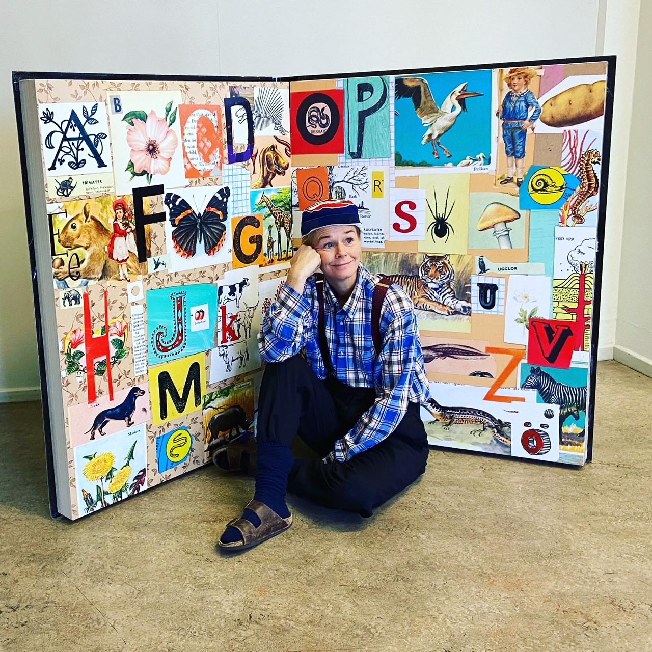 En person sitter framför en stor bok med bokstäver och bilder.