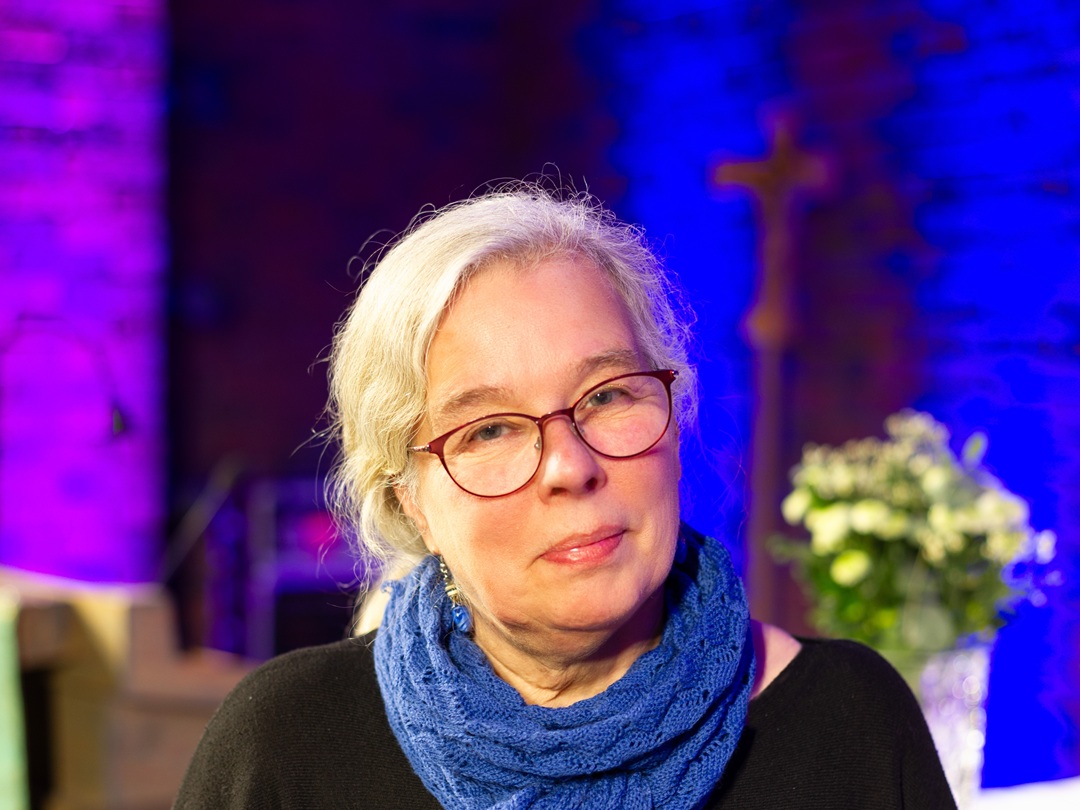 Unni Wiig Sandberg framför lila svart bakgrund och en bukett blommor