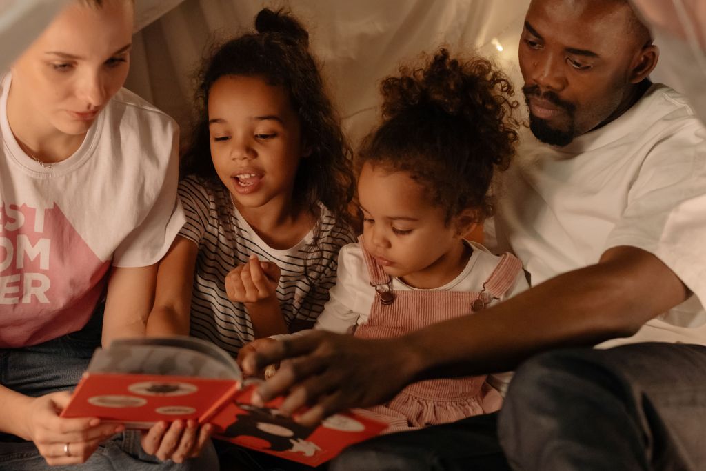 Två barn sitter med sin mamma och pappa och läser i en bok.