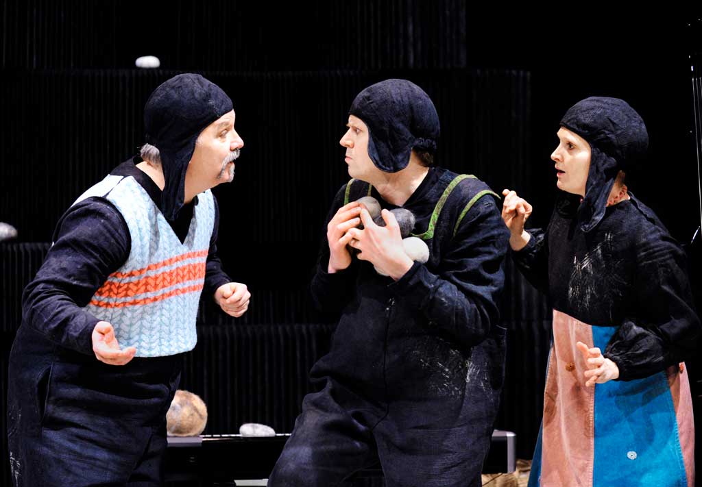 3 personer i svarta hättor. En av dem har stenar i famnen.