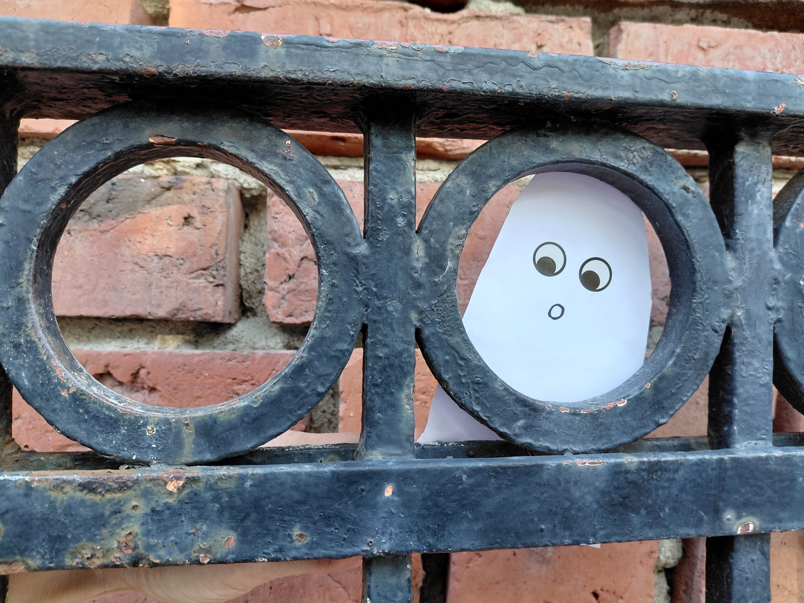 ett spöke som tittar fram bakom en svart järngrind.